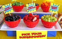 a table topped with red bowls filled with fruits and veggies next to buns