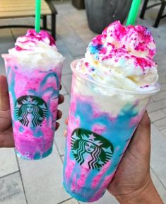 two people holding up drinks with pink and blue swirled toppings on the outside of them