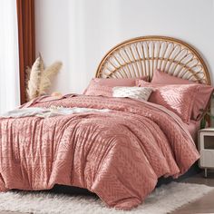 a bed with pink comforter and pillows in a room next to a wicker headboard