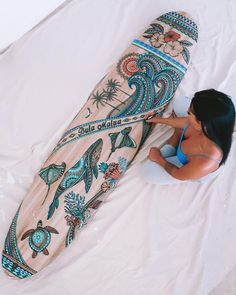 a woman laying on top of a bed next to a surfboard covered in tattoos