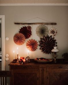 a table topped with lots of paper flowers next to a wall mounted art piece on top of a wooden cabinet