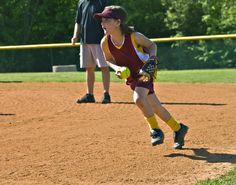 a girl running to catch a ball during a softball game with other people in the background