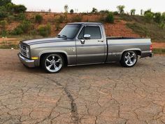 a silver truck parked in a parking lot next to a dirt hill covered with trees