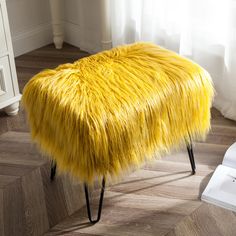 a bright yellow bench with black legs on wooden floor next to white dresser and window