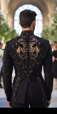 the back of a man wearing a black suit with gold embroidery on his chest and shoulders