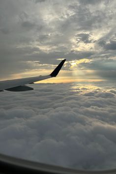 the wing of an airplane as it flies through the sky with clouds and sun in the distance