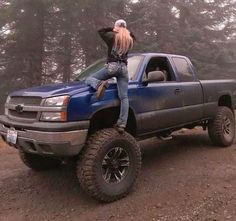 a woman sitting on the back of a blue truck with her arms in the air