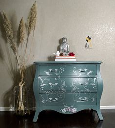 a green painted dresser next to a vase with flowers and a buddha statue on top