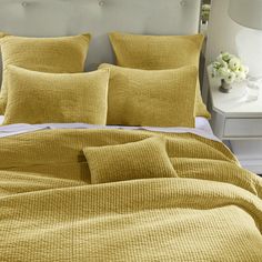 a bed with yellow sheets and pillows on top of it, next to a night stand