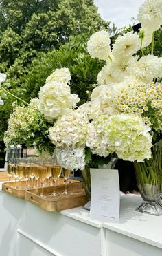 white flowers in vases and wine glasses on display at an outdoor wedding reception table