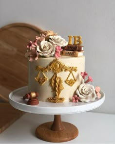 a cake decorated with gold and white flowers is on a plate next to a wooden chair