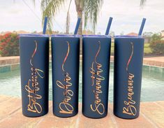 three blue tumblers with gold lettering on them sitting next to a pool and palm tree