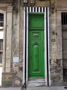 a green door is on the side of an old building with white and black stripes