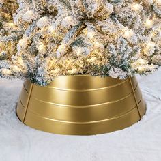 a christmas tree in a gold pot with snow on the ground and white fur around it