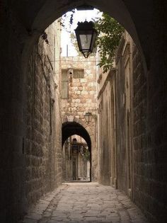 an alley way with stone walls and cobblestone walkway leading to a street light