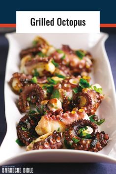 an octopus dish is served on a white platter with lemon wedges and parsley