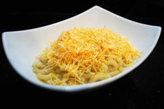 a white bowl filled with pasta and cheese on top of a black countertop next to a knife