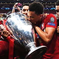 two soccer players are kissing the trophy while another man is taking a photo behind them