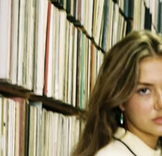 a woman with long hair standing in front of a bookshelf full of cds