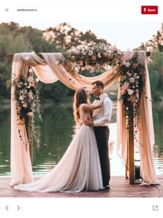 a bride and groom standing on a dock in front of an arch decorated with flowers