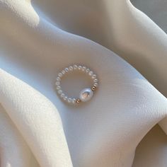 Delicate elastic fresh water pearl ring with 14kt gold filled beads. Carefully selected and high quality lustrous pearls make the ring truly beautiful and one of a kind. The delicate and minimalist design of the ring goes well with both casual and sophisticated looks. Size of the small pearl beads is approx. 2-2.5mm Size of the center large bead: 6x8mm Size of the gold filled bead: 2.5mm Follow us on INSTAGRAM: @soellejewelry Tag us on social media: #soellejewelry Packed with care and ready to s Pearl Ring Handmade, Diy Beads Ring Ideas, Pearl Beaded Ring, Ring Ideas Diy Bead, Ring Designs Beads, Silver Ring With Pearl, Pearl White Ring With Pearl Chain, Elegant Adjustable Pearl Ring, White Pearl Ring With Pearl Chain