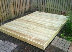 a wooden platform sitting in the middle of a yard next to a brick walkway and fence