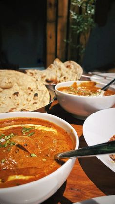 several bowls of food on a table with bread and pita bread in the background