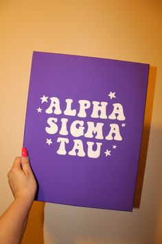 a person holding up a purple sign with white letters on it that says, alpha sigma tau