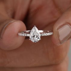 a woman's hand holding an engagement ring with a pear shaped diamond on it