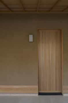 an open wooden door in front of a tan wall with wood slats on it