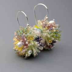 two pairs of beaded earrings with pearls and beads hanging from hooks on a gray surface