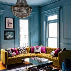 a living room with blue walls and yellow couches in front of two windows that have pictures on them