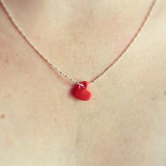 a woman wearing a necklace with a red heart pendant on it's back neck