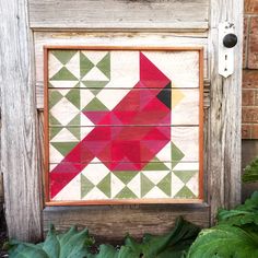 a red bird painted on wooden planks in front of a brick wall and green plants