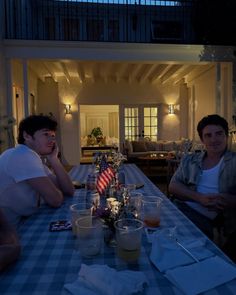 two men sitting at a table with an american flag in the middle and another man standing next to them