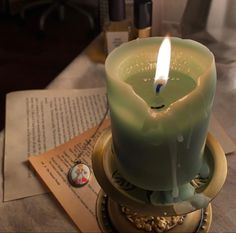 a lit candle sitting on top of a table next to an open book and pen