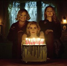 three women standing in front of a cake with candles on it