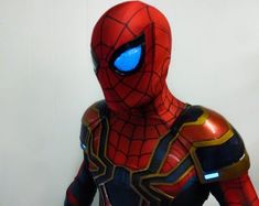 a man in a spider - man suit with glowing blue eyes is standing next to a white wall