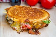 a grilled cheese sandwich sitting on top of a wooden cutting board next to tomatoes