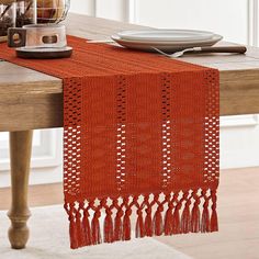 an orange table runner with tassels on it and a plate in the background