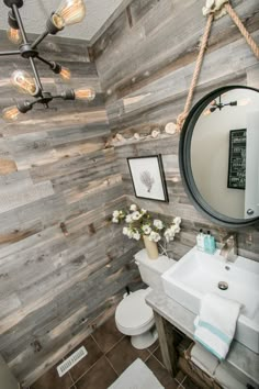 the bathroom is decorated with wood planks and white porcelain fixtures, including a round mirror