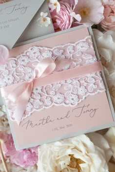 a pink and white wedding card with a ribbon on it, surrounded by flower petals