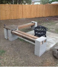 a concrete bench with a fire pit in the middle and a wooden fence behind it