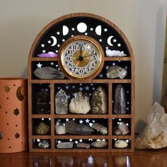 a clock sitting on top of a wooden shelf filled with rocks and other items next to a vase