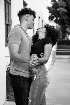 a man and woman standing next to each other on a sidewalk with their noses close together