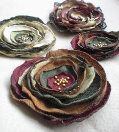 four flower brooches sitting on top of a white cloth covered table next to each other