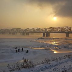 some people are standing in the snow and ice near a bridge that is over water