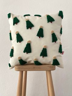 a white pillow with green trees on it sitting on top of a wooden stool next to a wall