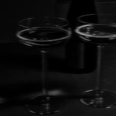 two wine glasses sitting next to each other in front of a bottle and black background