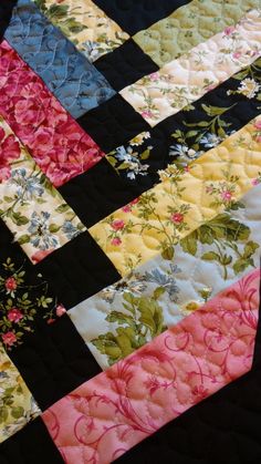 a close up of a quilt on a bed with black and pink flowers in the center